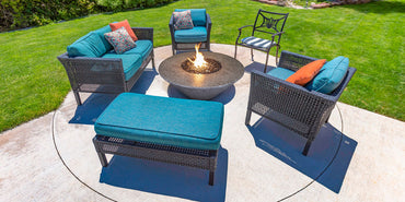 Outdoor patio set with blue cushions and a fire pit table on a grassy area.