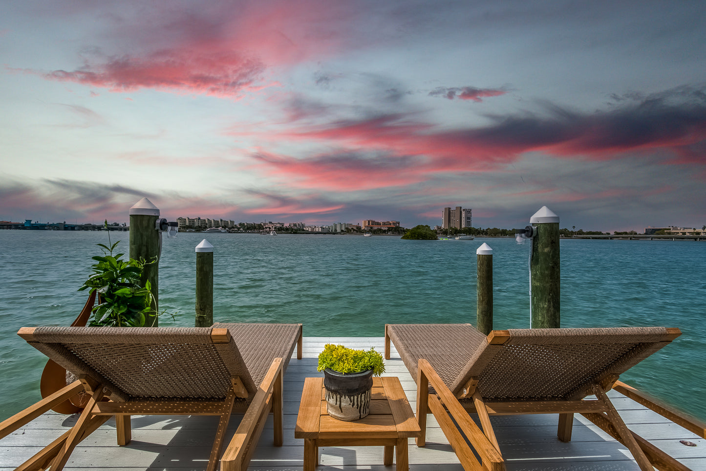 Two lounge chairs on a dock with a scenic view of water and city skyline at sunset.