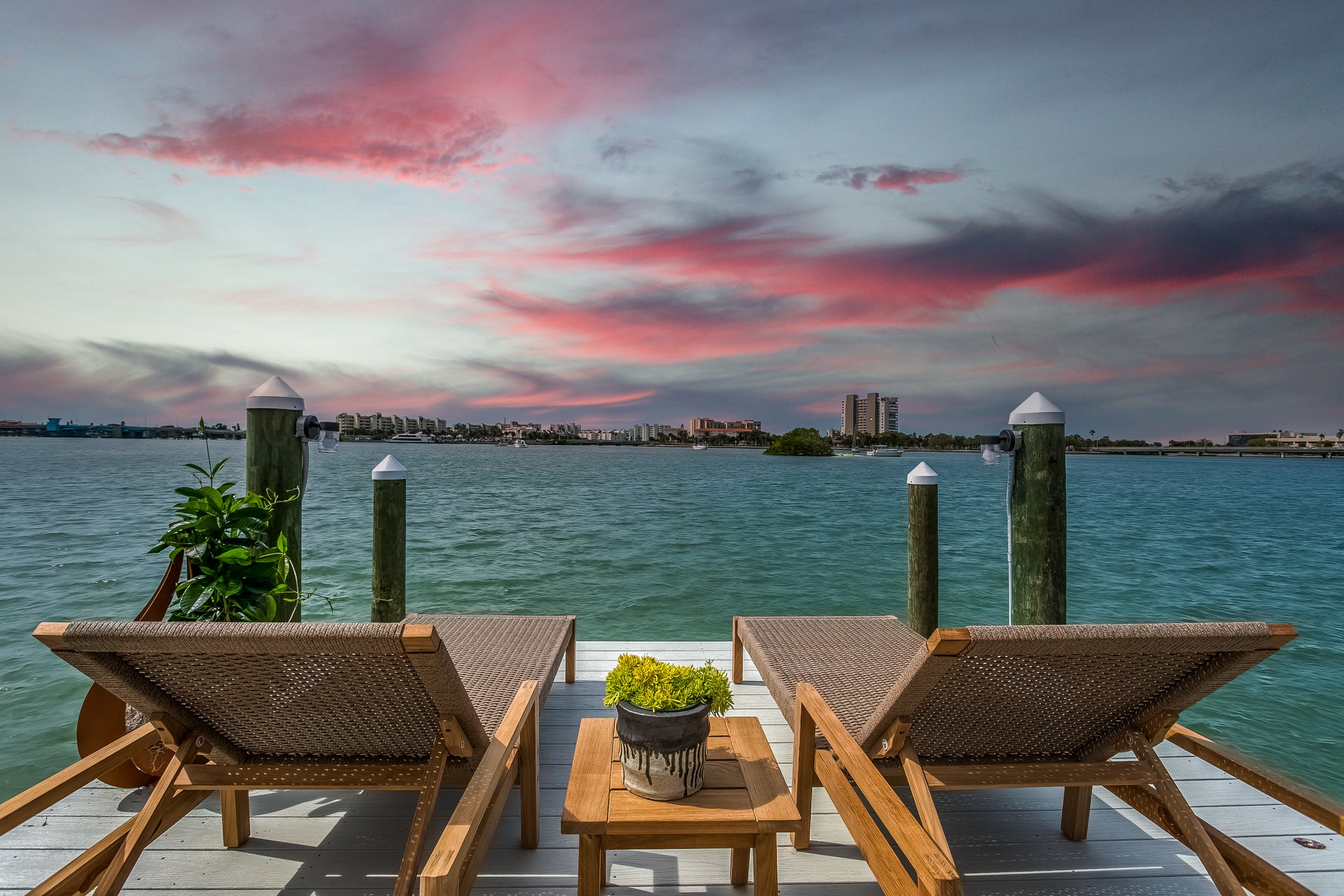Two lounge chairs on a dock with a scenic view of water and city skyline at sunset.
