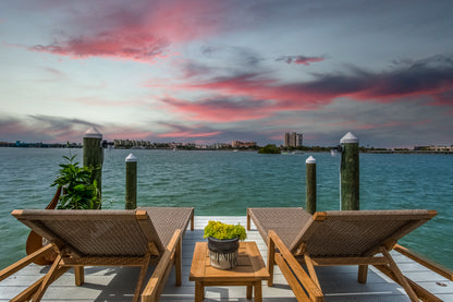 Two lounge chairs on a dock with a scenic view of water and city skyline at sunset.