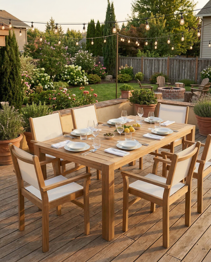 Outdoor dining setup with wooden table and chairs on a wooden deck, surrounded by garden and string lights.