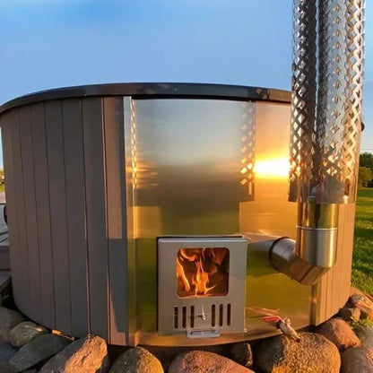 Portable stove with flames inside, surrounded by stones and grass with a sunset in the background.