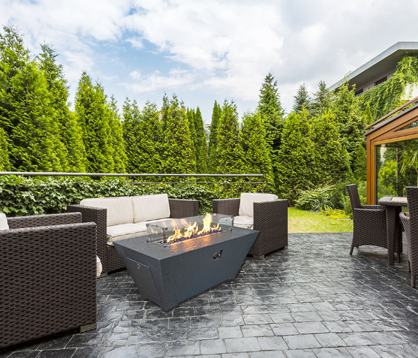 Outdoor patio with fire pit, chairs, and a gazebo in a garden setting.