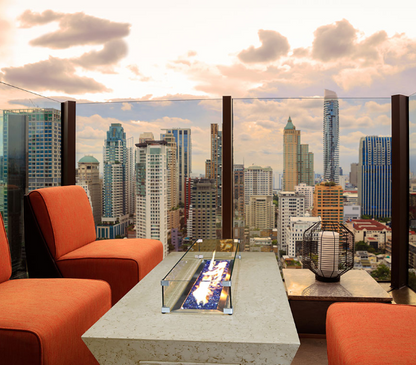 Outdoor seating area with a fire pit table and orange chairs, overlooking a city skyline.