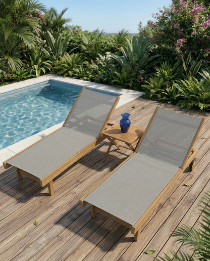 Two wooden lounge chairs with gray cushions on a wooden deck by a pool, surrounded by greenery.