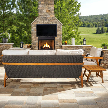 Outdoor patio with stone fireplace, TV, and wicker furniture in a scenic setting.