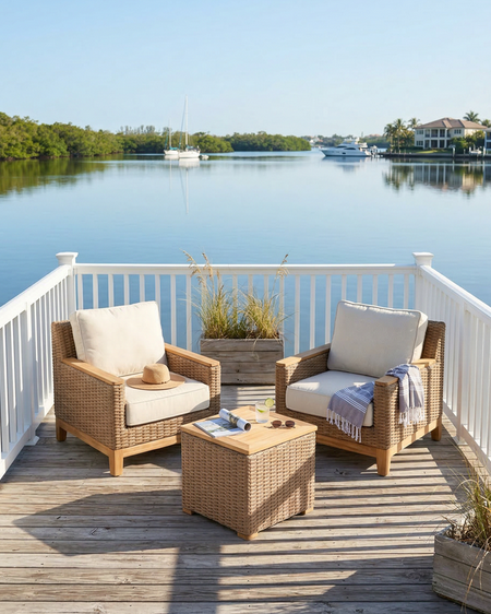 Outdoor patio set with wicker chairs and table on a deck overlooking a body of water.