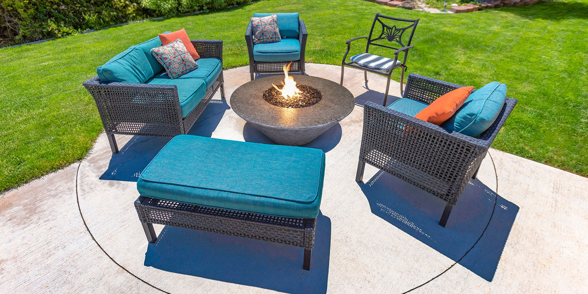 Outdoor patio set with blue cushions and a fire pit table on a grassy area.